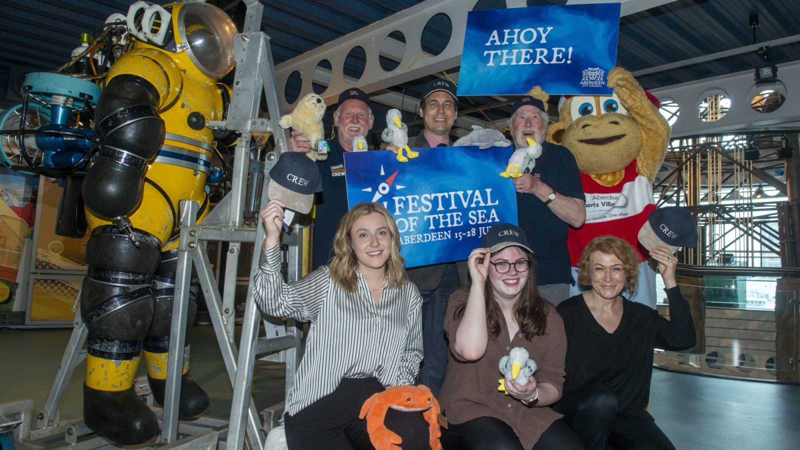 Councillor Martin Greig, culture spokesperson for Aberdeen City Council,  with Wishart McBride, David Brown, RNLI fundraising volunteers along with Mhairi McBeath, Deemouth Artists Studio, Sarah Boyle, Open Road, Lesley Anne Rose, Open Road Creative Director and with Aberdeen Sports Village mascot ASVIL.